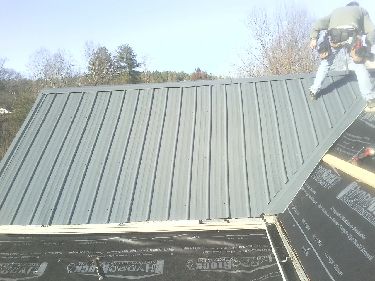 Crew installing dark green standing seam panels over synthetic underlayment in Avalon
