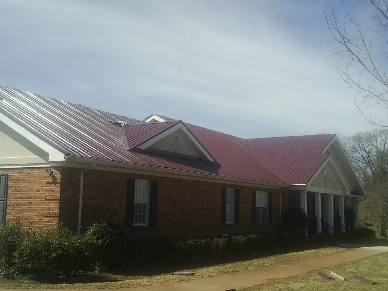 Red metal roof with gabled entries on a long brick building, from a Hail Damage Roof Repair job in Avalon